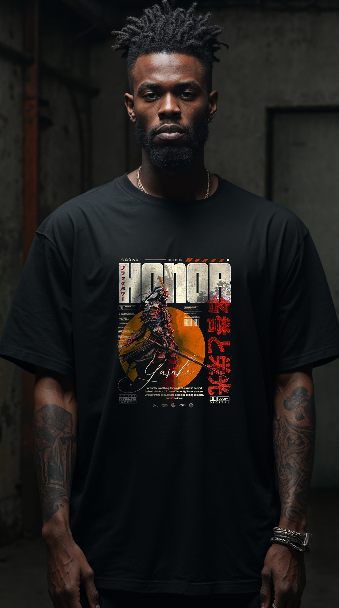 Homme barbu aux bras tatoués portant le t-shirt noir oversize HONOR, graphic Yasuke samouraï japonais orange bien visible, vue portrait corps entier, streetwear inspiré du samouraï noir