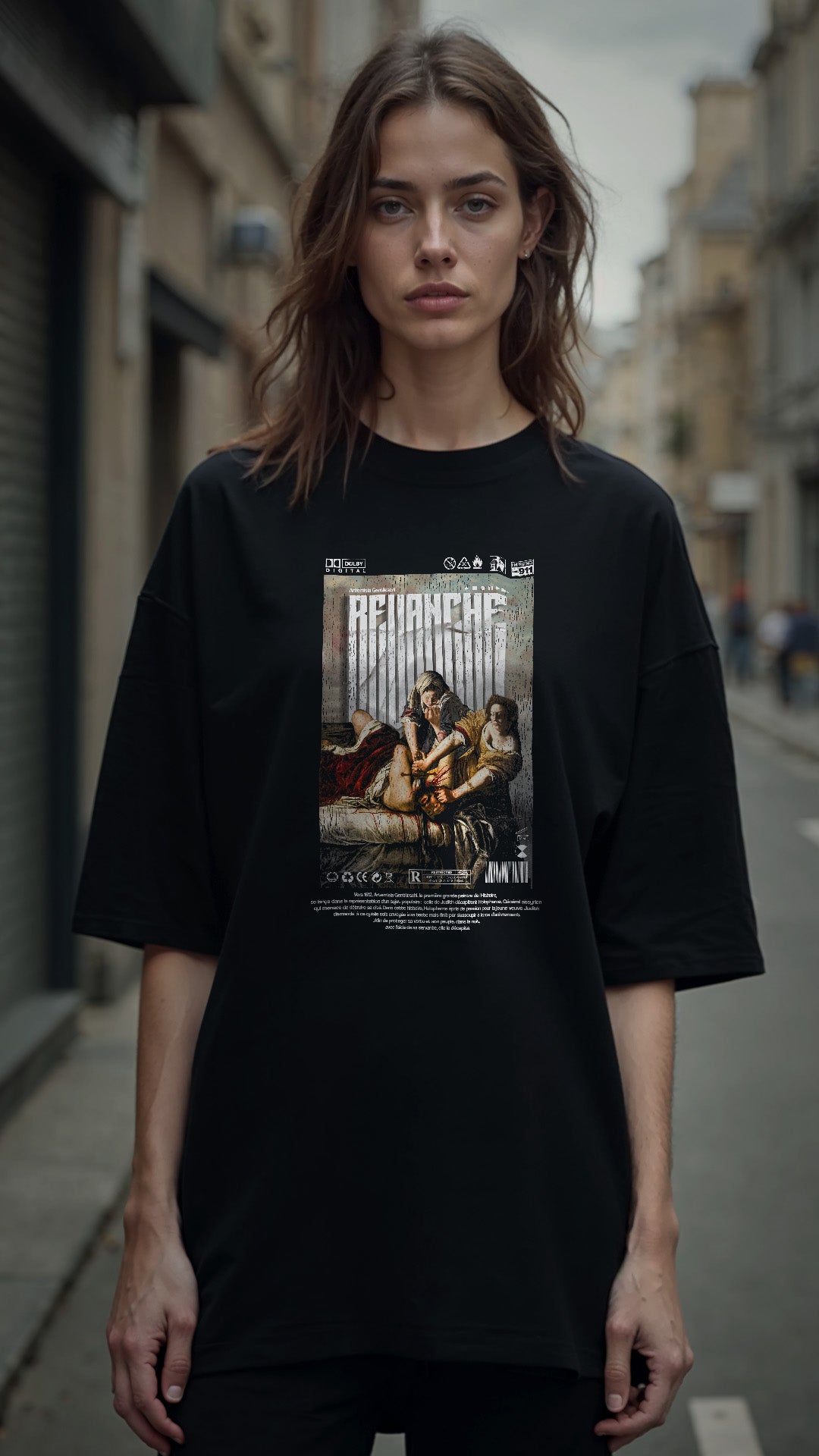T-shirt noir REVANCHE inspiré du tableau d’Artemisia Gentileschi vu de face avec graphic imprimé sur le devant, porté par femme ambiance cinématographique, style streetwear vintage, fond street bokeh