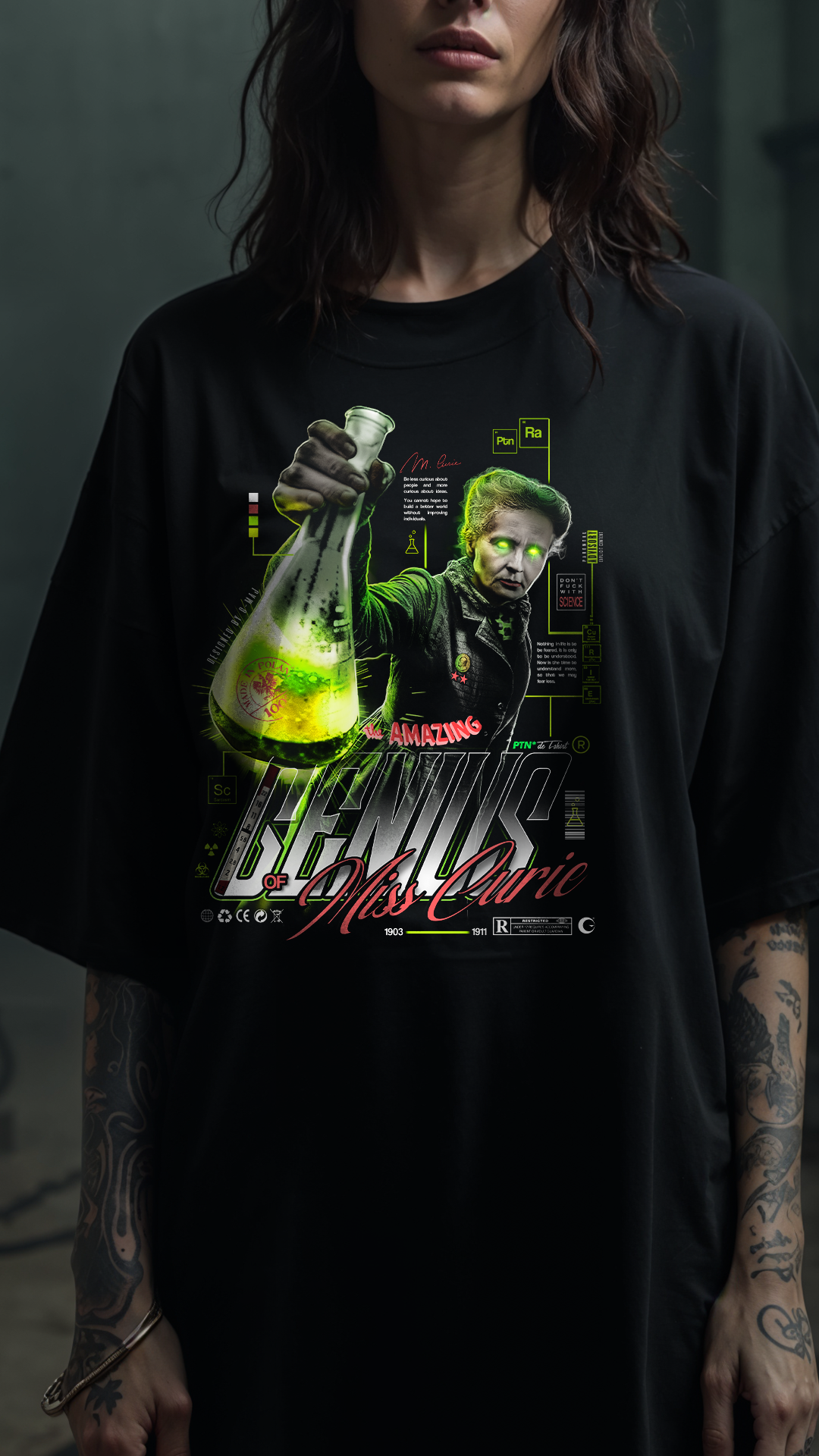 Vue rapprochée du graphic GENIUS PTN* DE T-SHIRT sur t-shirt noir oversize, design Marie Curie tenant un flacon vert lumineux bien visible, porté par une personne aux bras tatoués